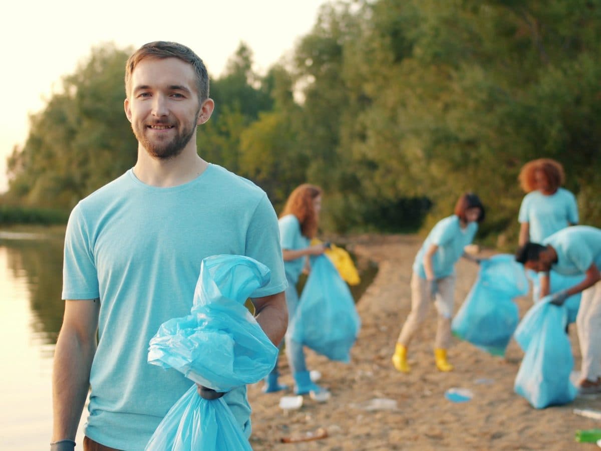 Un salarié souriant, sac de collecte à la main, sur une berge